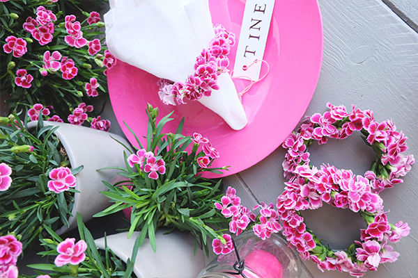 Selbstgemachte Serviettenringe aus den pinkfarbenen Blüten der Pink Kisses Mininelke, daran mit farblich passendre Schnur eine kleine Karte mit Namen darauf als Platzkärtchen